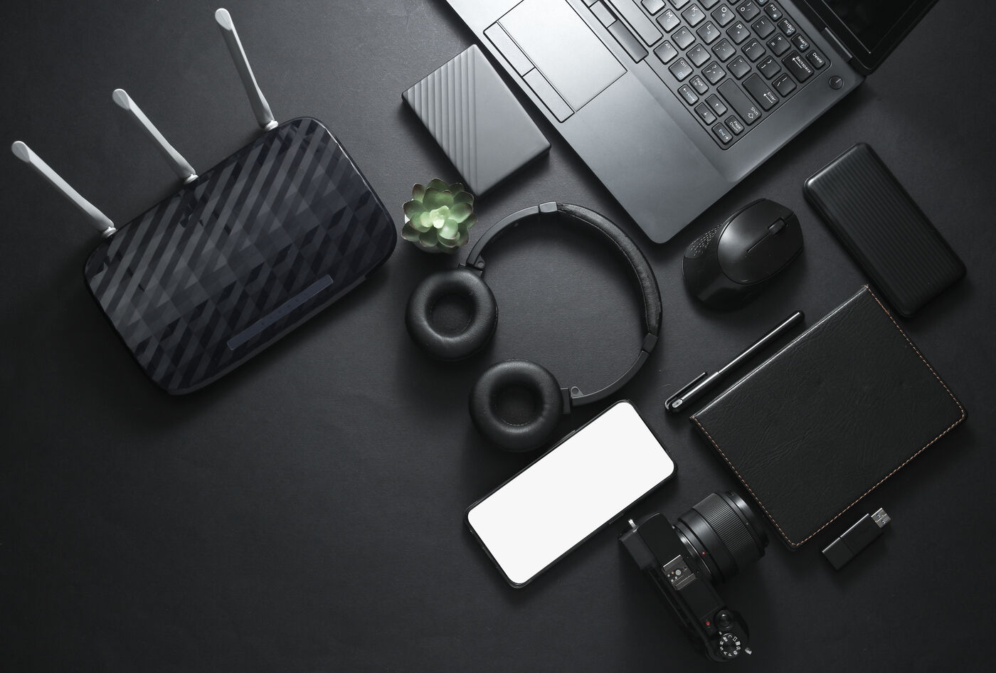 Notebook, router, auriculares, celular y otros dispositivos sobre una mesa oscura